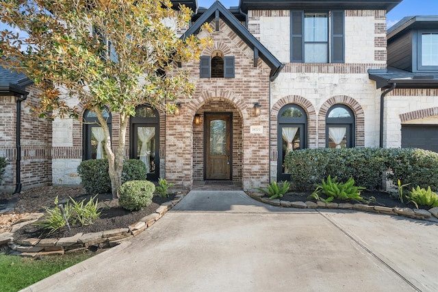 doorway to property featuring a garage, stone siding, and brick siding