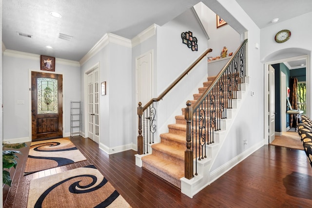 entryway featuring arched walkways, crown molding, visible vents, baseboards, and hardwood / wood-style flooring