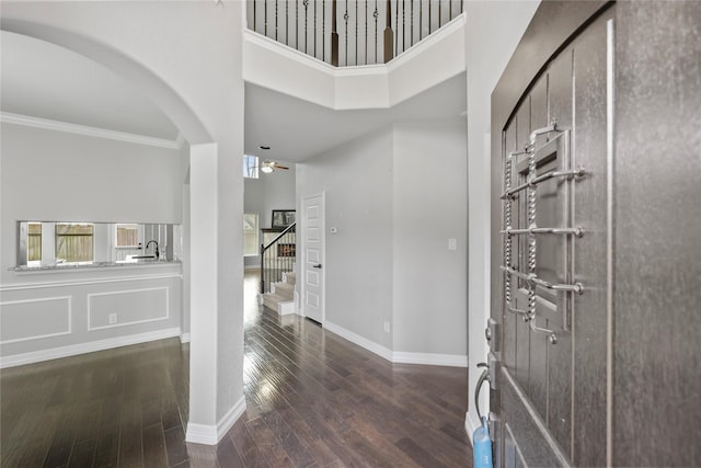 foyer with wood finished floors, a towering ceiling, baseboards, ornamental molding, and stairway