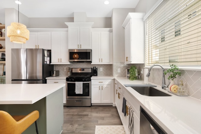 kitchen with light countertops, backsplash, appliances with stainless steel finishes, white cabinetry, and a sink