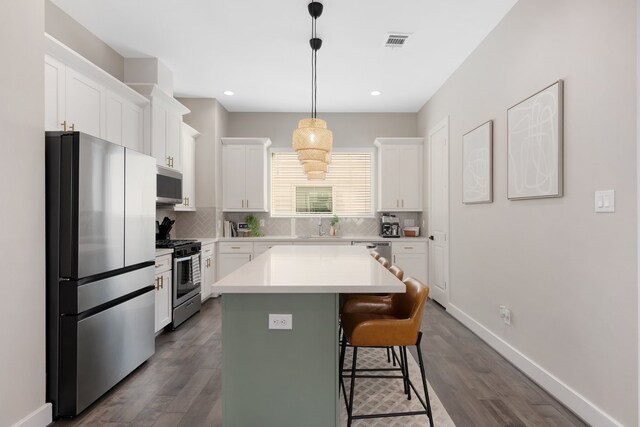 kitchen featuring visible vents, white cabinets, decorative backsplash, appliances with stainless steel finishes, and a breakfast bar area