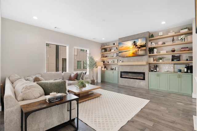 living room featuring light wood-type flooring, a glass covered fireplace, visible vents, and recessed lighting