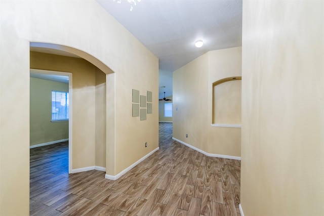 hall with arched walkways, wood finished floors, and baseboards