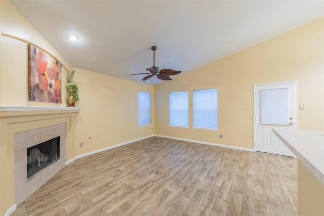 unfurnished living room featuring lofted ceiling, a tiled fireplace, light wood-style floors, a ceiling fan, and baseboards