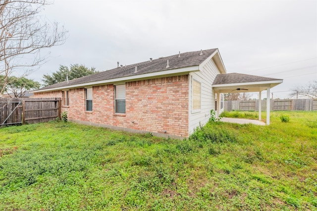 view of property exterior featuring ceiling fan, fence, a lawn, and brick siding