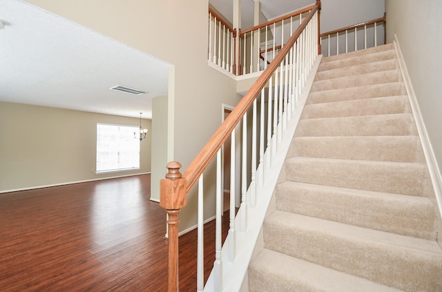 stairs featuring an inviting chandelier, visible vents, baseboards, and wood finished floors