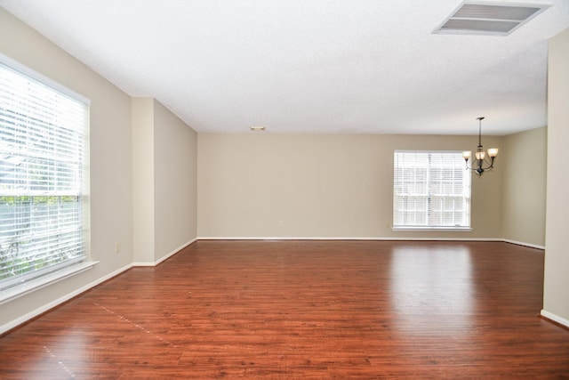 empty room featuring visible vents, a notable chandelier, baseboards, and wood finished floors