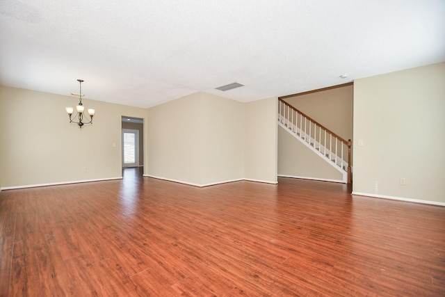 unfurnished living room with stairs, visible vents, a notable chandelier, and wood finished floors