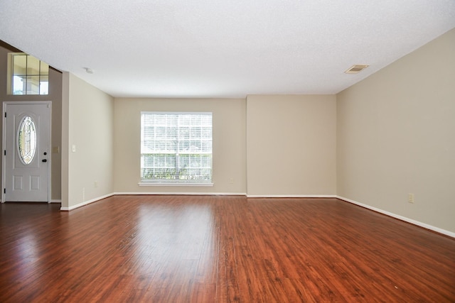 interior space with baseboards, a textured ceiling, visible vents, and dark wood-type flooring