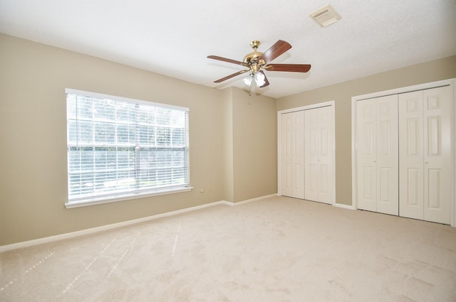 unfurnished bedroom with light carpet, a ceiling fan, visible vents, baseboards, and two closets