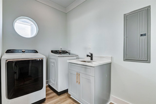 clothes washing area with washer and clothes dryer, light wood finished floors, cabinet space, a sink, and electric panel