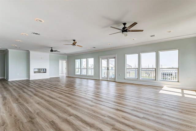 unfurnished living room with a fireplace, visible vents, wood finished floors, and ornamental molding