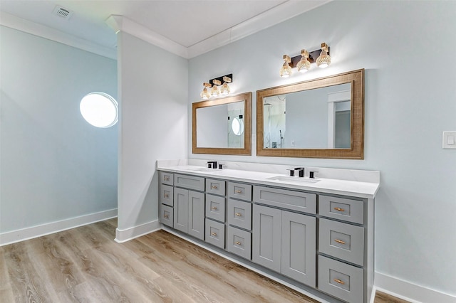 bathroom featuring wood finished floors, visible vents, baseboards, ornamental molding, and double vanity