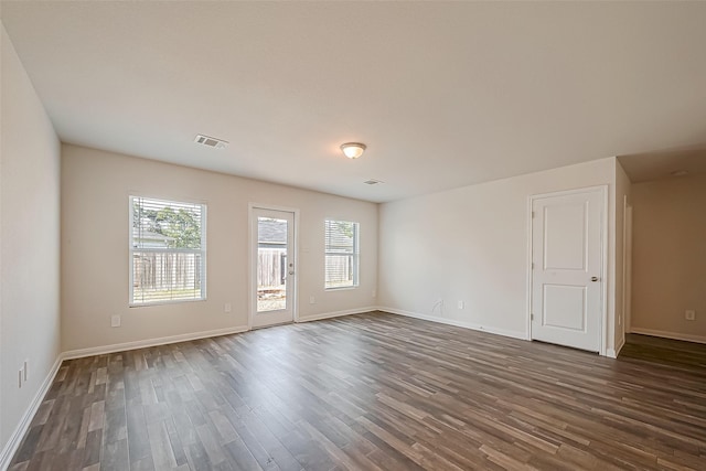 empty room featuring dark wood-style floors, visible vents, and baseboards