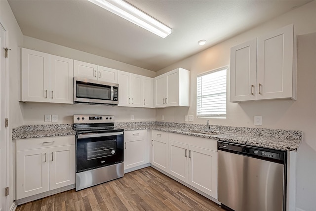 kitchen with light wood finished floors, white cabinets, light stone counters, appliances with stainless steel finishes, and a sink