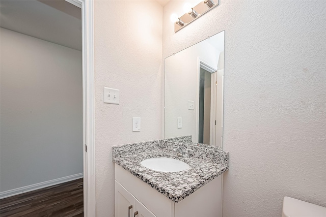 bathroom with baseboards, a textured wall, toilet, wood finished floors, and vanity