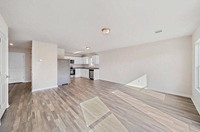 unfurnished living room with light wood-style floors, visible vents, and baseboards