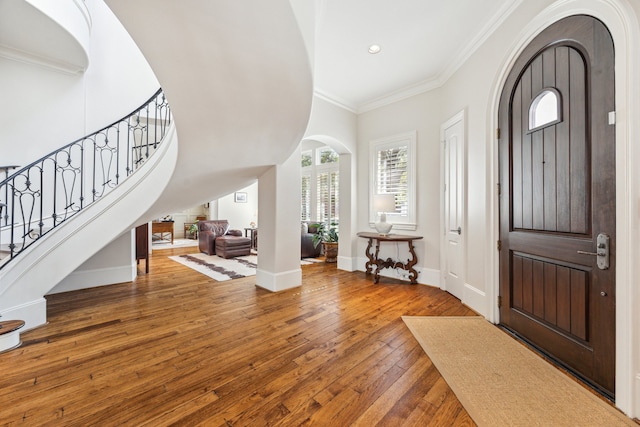 foyer entrance featuring arched walkways, baseboards, wood-type flooring, stairway, and ornamental molding