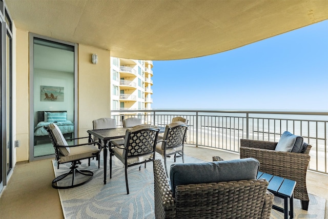 balcony featuring outdoor dining space, a water view, and a beach view