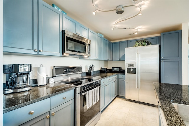 kitchen with blue cabinets, dark stone counters, stainless steel appliances, and light tile patterned flooring