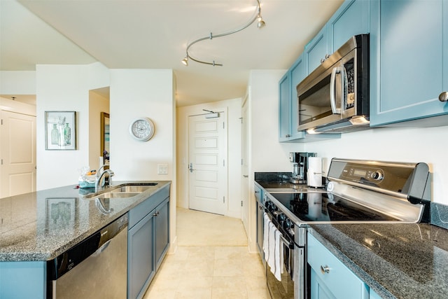 kitchen featuring blue cabinets, dark stone countertops, appliances with stainless steel finishes, and a sink