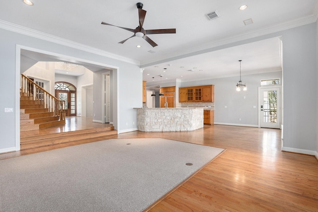 unfurnished living room with crown molding, visible vents, plenty of natural light, and stairs