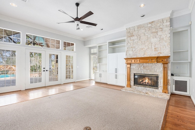 unfurnished living room with built in features, french doors, wood finished floors, crown molding, and a stone fireplace