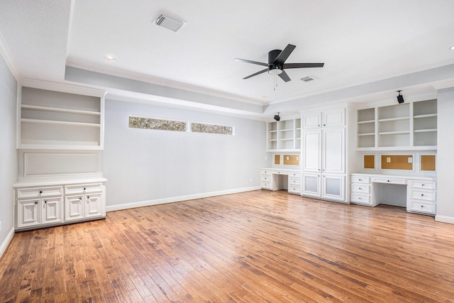 unfurnished living room featuring a tray ceiling, built in desk, visible vents, baseboards, and hardwood / wood-style flooring