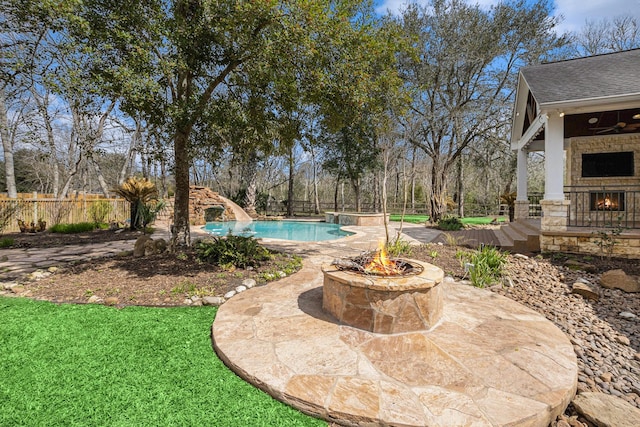 view of pool with a water slide, an outdoor stone fireplace, fence, a fenced in pool, and a patio area