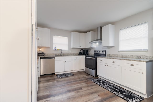 kitchen with stainless steel appliances, white cabinetry, a sink, and wall chimney range hood