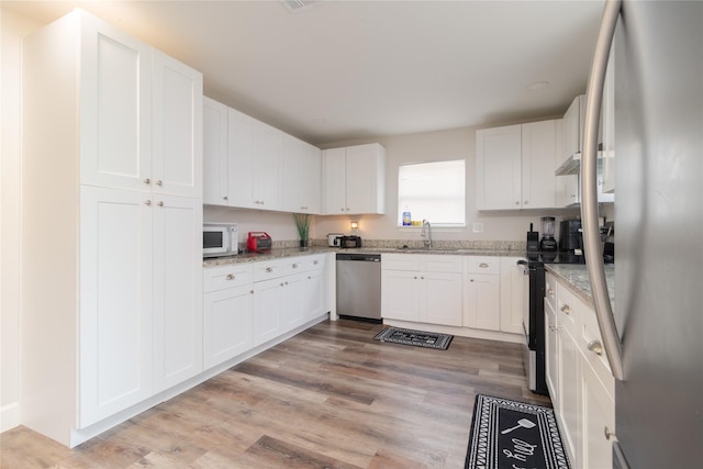 kitchen with stainless steel appliances, light wood finished floors, white cabinetry, and light stone counters