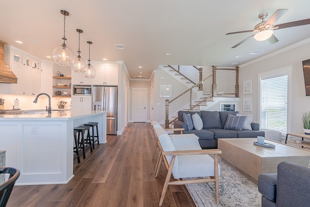 living room with stairway, visible vents, dark wood-style flooring, and ornamental molding