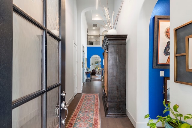 corridor featuring arched walkways, a towering ceiling, visible vents, baseboards, and dark wood finished floors