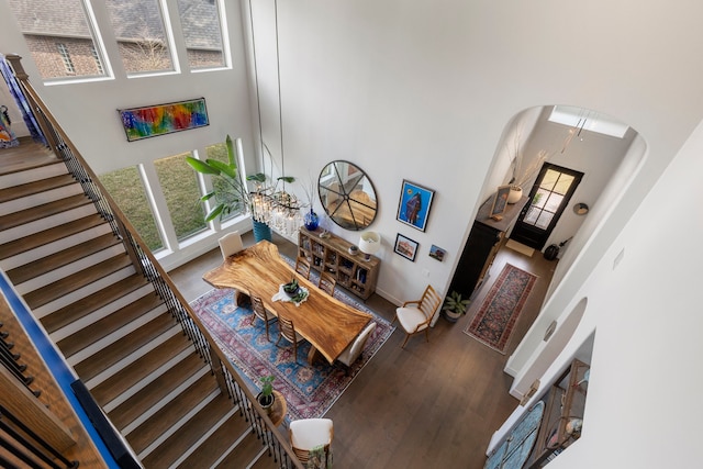 living area with arched walkways, a high ceiling, stairway, and wood finished floors