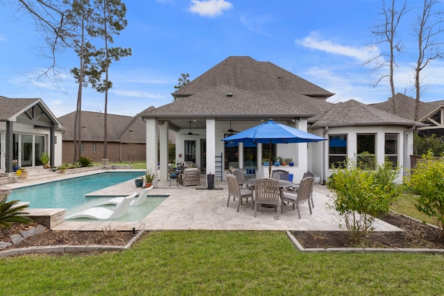 rear view of property with a patio, a ceiling fan, a yard, roof with shingles, and an outdoor pool