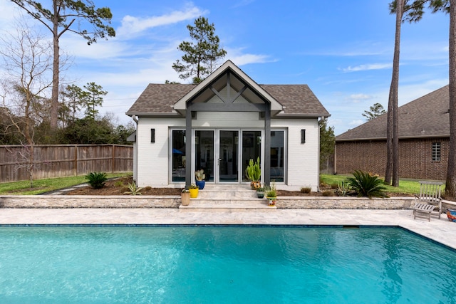 rear view of property featuring roof with shingles, fence, and a fenced in pool