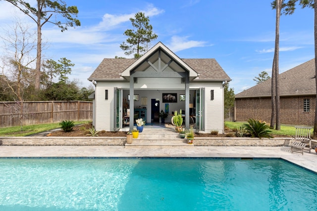 rear view of house featuring a fenced in pool, an outbuilding, roof with shingles, and fence