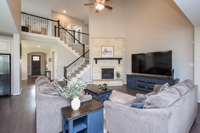 living area featuring a fireplace, a towering ceiling, dark wood-type flooring, baseboards, and stairs