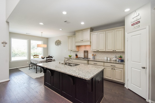 kitchen with stainless steel gas cooktop, cream cabinetry, a sink, and tasteful backsplash