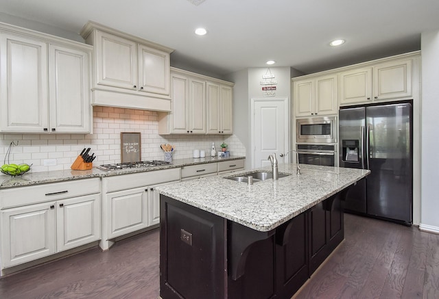 kitchen featuring dark wood finished floors, decorative backsplash, appliances with stainless steel finishes, a sink, and light stone countertops