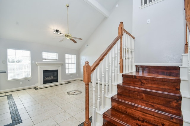 staircase featuring ceiling fan, high vaulted ceiling, a glass covered fireplace, and tile patterned floors