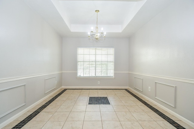 spare room featuring a tray ceiling, a decorative wall, a chandelier, baseboards, and tile patterned floors