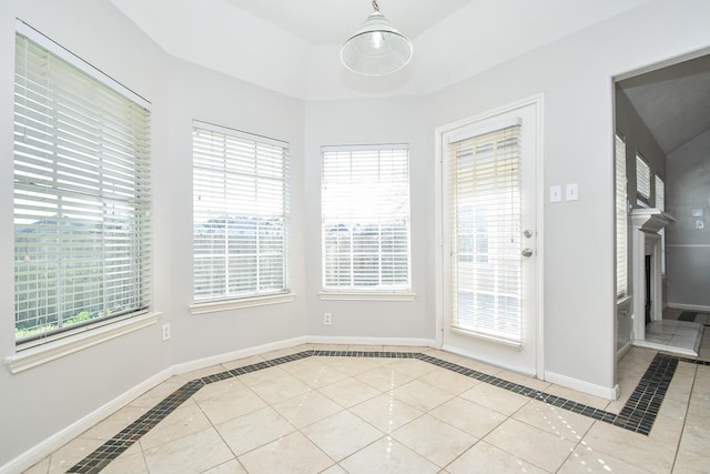 unfurnished dining area with a tray ceiling, a fireplace, baseboards, and tile patterned floors