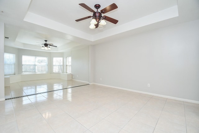 empty room featuring light tile patterned floors, a raised ceiling, a ceiling fan, and baseboards