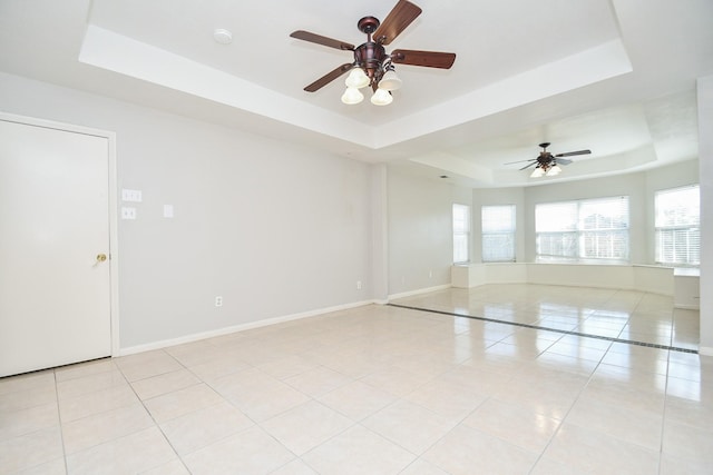 empty room featuring a tray ceiling, light tile patterned flooring, ceiling fan, and baseboards