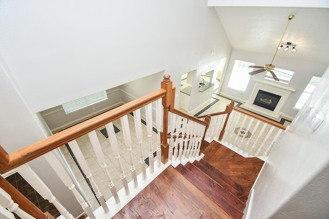 staircase with a glass covered fireplace, wood finished floors, and a ceiling fan