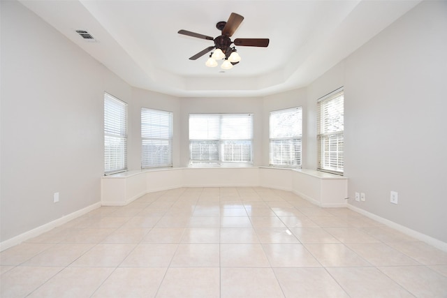 spare room featuring a tray ceiling, light tile patterned floors, visible vents, a ceiling fan, and baseboards