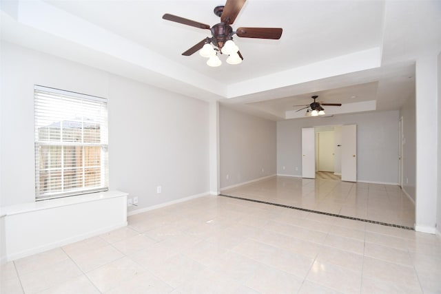 spare room with light tile patterned floors, ceiling fan, baseboards, and a raised ceiling