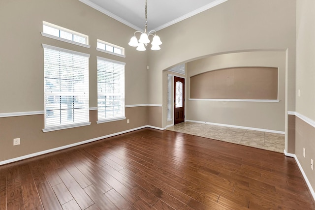 unfurnished room featuring baseboards, arched walkways, ornamental molding, wood finished floors, and an inviting chandelier