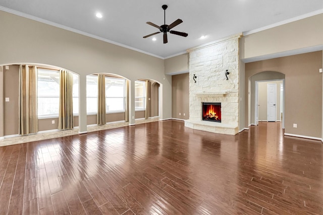 unfurnished living room with baseboards, ceiling fan, wood finished floors, crown molding, and a stone fireplace